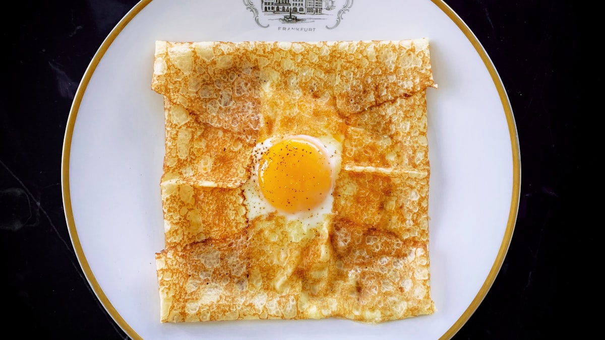 A jianbing breakfast crepe being folded on a flat griddle